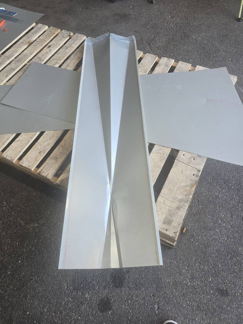 Long white metal valley flashing and flat white panels laid on a wooden pallet in a driveway