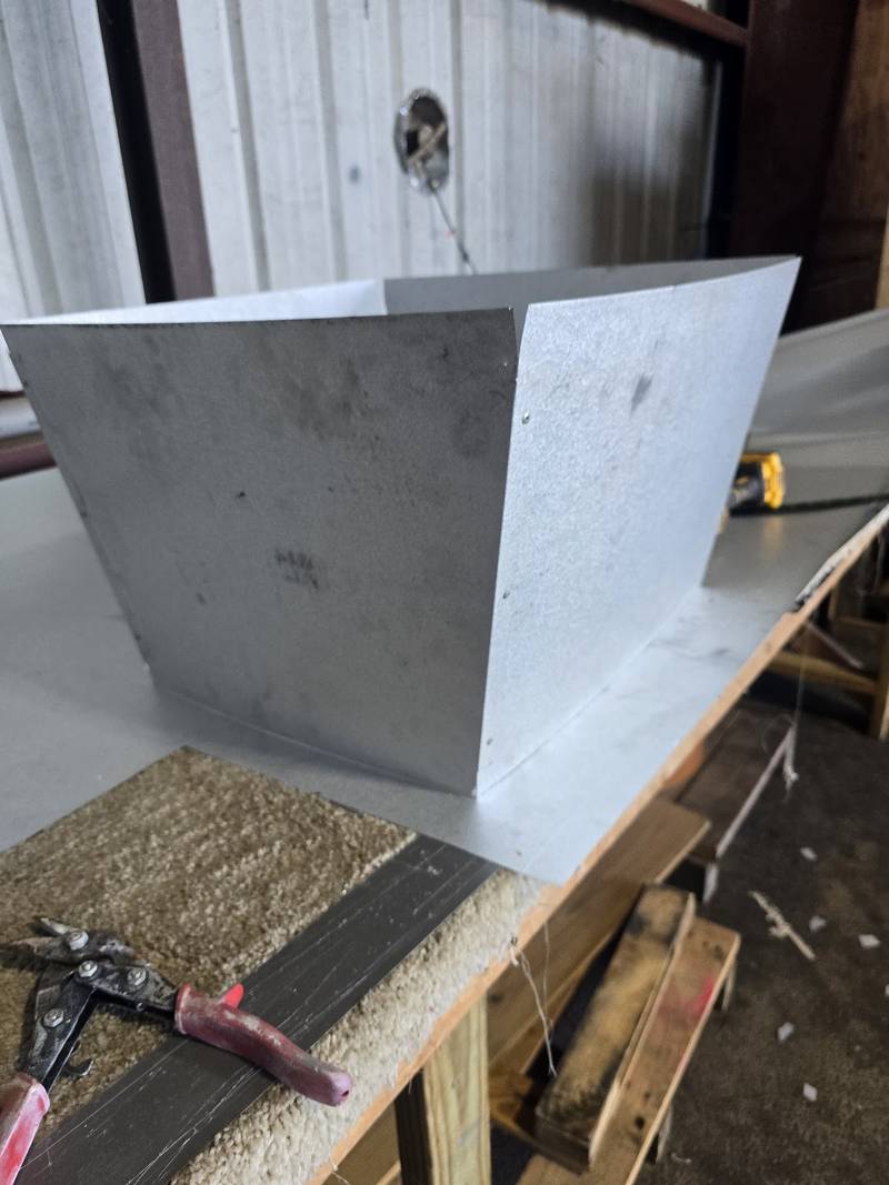 Bent galvanized sheet-metal piece on a plywood workbench with red-handled tin snips and a yellow tape measure