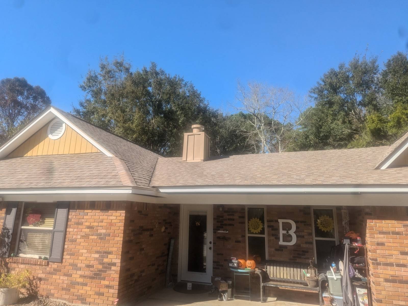 Front of a one-story brick house with a tan architectural-shingle roof, a yellow board-and-batten gable and a boxed chimney under blue sky
